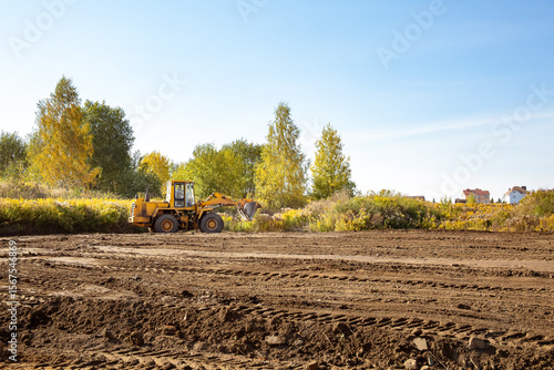 Yellow bulldozer at a construction site. Big wheel excavator leveling and clearing the land plot side view. Moving earthworks soil. Copy space. Building area. Special transport. High quality photo.