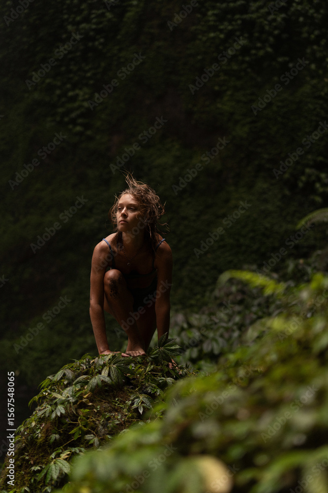 Young woman crouching on moss-covered rock in lush rainforest Young woman crouching on moss-covered rock in lush rainforest