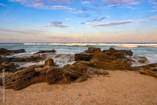 Fototapeta Naklejka Na Ścianę i Meble -  A beach of coquina rocks is sculpted by the sea in this evening landscape view with soft water at River to Sea Preserve