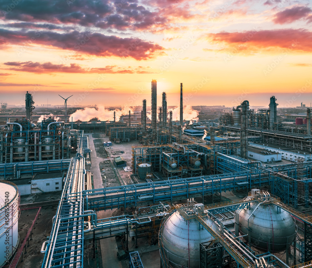 Obraz premium Large oil refinery and industrial petrochemical plant complex under colorful sunset sky.