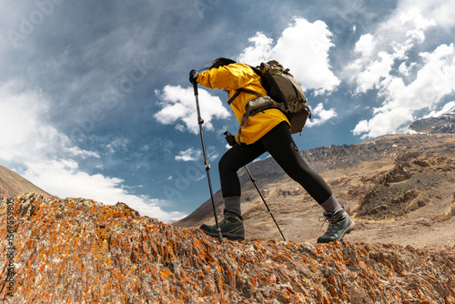 Girl trekker in hiking gear climbs a rock against the background of blue sky with clouds and rocky Altai mountains. Low angle bottom view. Adventure energy, endurance, solo hike
