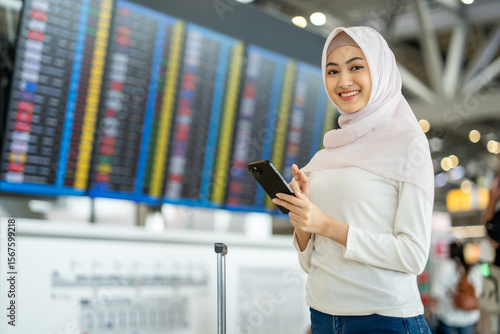 Canvas Print Muslim asian businesswoman traveler holding boarding pass ticket, passport and smartphone at the airport terminal with her luggage