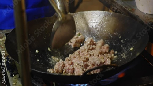 Close-up shots of stir-frying minced meat with red chili peppers in a hot wok over an open flame, with visible smoke and fire during cooking