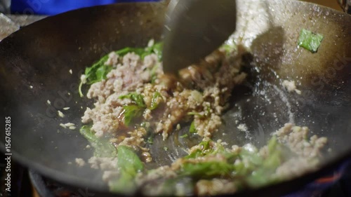 Close-up shots of stir-frying minced meat with red chili peppers in a hot wok over an open flame, with visible smoke and fire during cooking