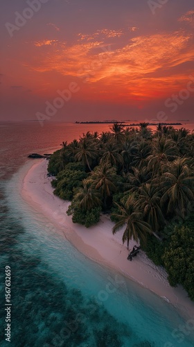Aerial view of a tropical island at sunset.  A pristine white sand beach is fringed by lush green vegetation and palm trees.  A vibrant coral-hued sunset paints the sky above the tranquil ocean
