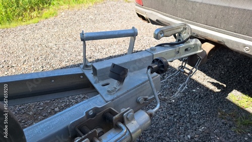 Photography Close-up of metal trailer hitch attached to car on gravel surface