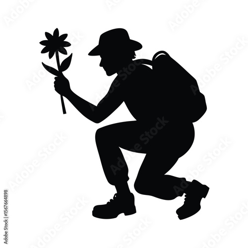 Black silhouette of hiker squatting holding flower
