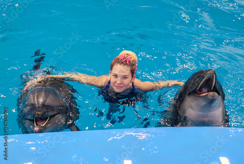 Woman interacts with dolphins in a blue pool during a marine park encounter