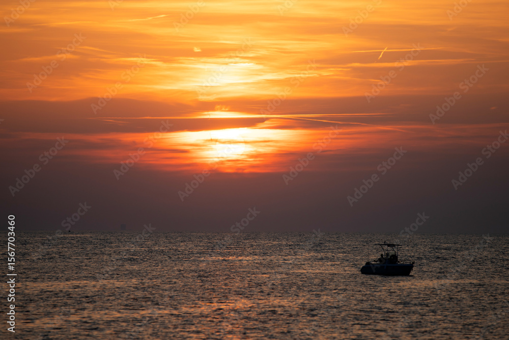 Obraz premium Boat silhoutted against the orange sky