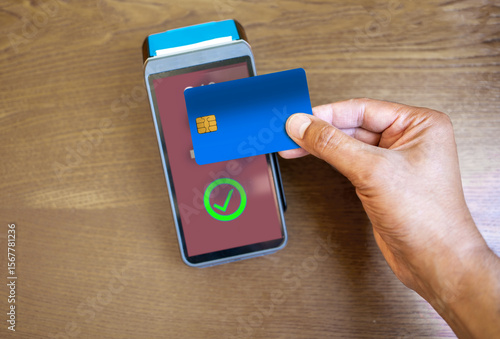 Photography Clerk accepting a contactless blue credit card payment using nfc technology from a customer in a cafe or store