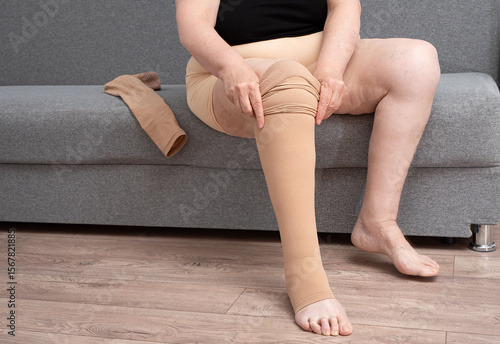 Mature plump woman putting on compression stockings on her legs. Vascular health