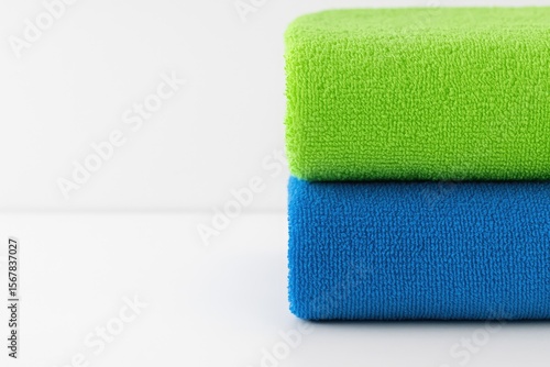 Detailed view of a partially stacked set of green and blue towels against a white backdrop with room for text