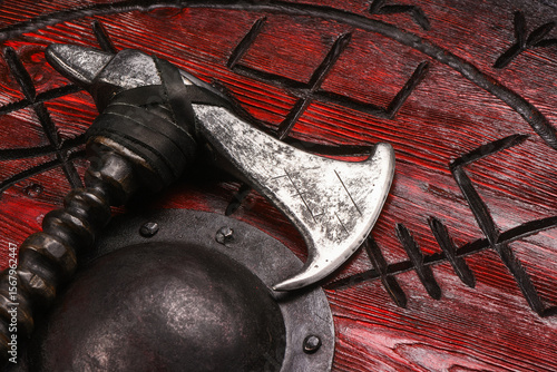 Medieval Viking axe and warrior red shield on old warrior table close up background.