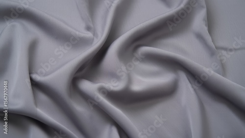 Luxurious silver gray silk fabric with flowing drapes and elegant folds creating soft shadows and smooth textile waves in natural lighting