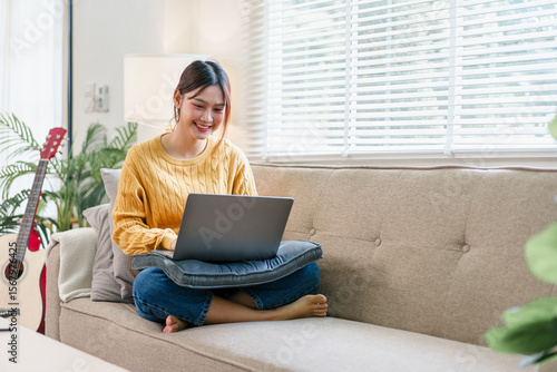 Φωτογραφία Young woman sitting cross legged on sofa with laptop, smiling and working in bri