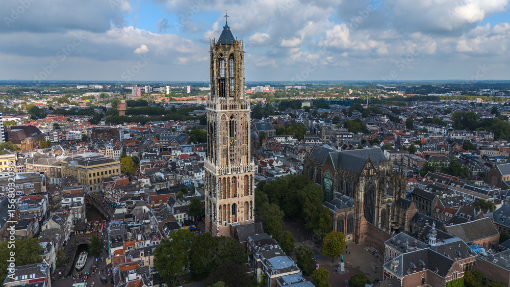 Fototapeta premium Drone photo of Utrecht’s Domtoren rising above the old city. The cathedral nave and canal streets sit around the tower, with the green Utrecht province stretching out behind. 