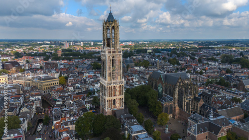 Drone photo of Utrecht’s Domtoren rising above the old city. The cathedral nave and canal streets sit around the tower, with the green Utrecht province stretching out behind.
