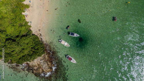 Top-down drone photo of a small beach and emerald-clear water at Ilha Grande, Rio de Janeiro state. Speedboats anchor in the shallow lagoon while swimmers relax near the sand. 