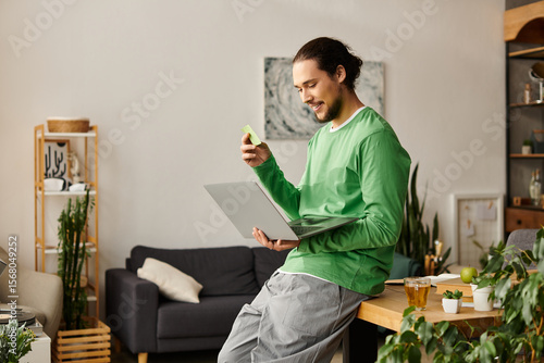 Young man enjoying leisure time at home while working on his laptop and snacking