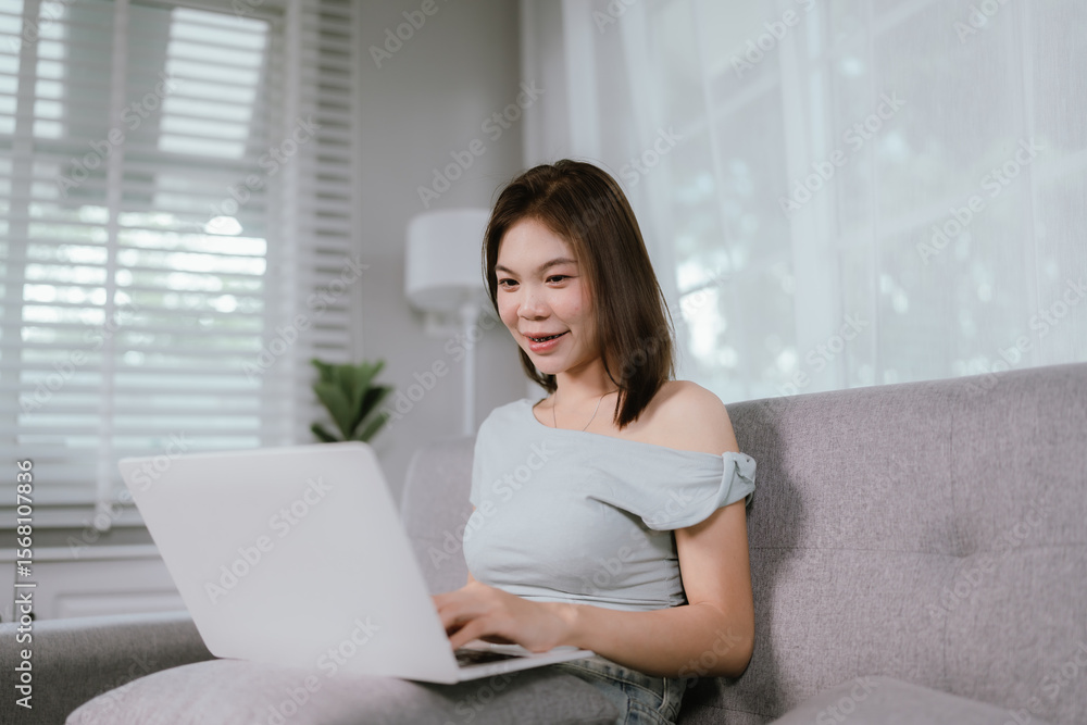 Asian woman makes online payments using credit card and laptop while sitting comfortably on sofa, managing finances or shopping from home. Asian woman makes online payments using credit card and laptop while sitting comfortably on sofa, managing finances or shopping from home.