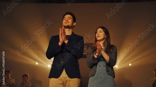 Young couple applauding during performance on stage with lights  