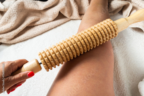 Hand holding a wooden massage roller during maderotherapy on the leg. Natural wellness and body care concept.