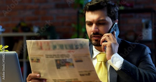 businessman reading business newspaper while sitting at modern computer desk, Indian Asian corporate executive focused on financial news, market updates, concept of awareness, leadership