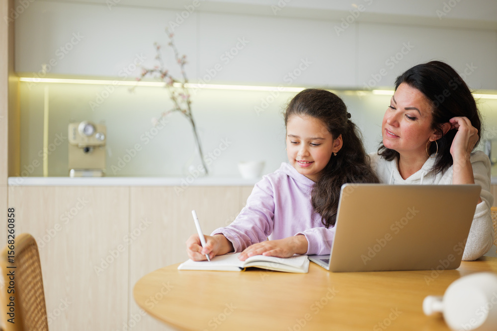 Obraz premium Mother and daughter sharing a creative study session at home on a cozy afternoon with notebooks and a laptop