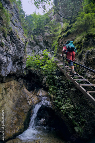 A hiker ascends a series of ladders alongside a waterfall in a narrow gorge.