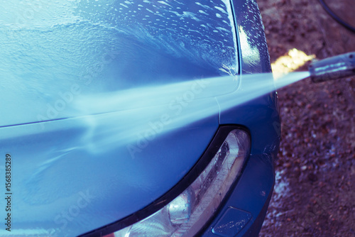 Car washing with high-pressure water spray at an outdoor facility on a sunny day