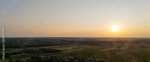 Obraz na płótnie Aerial view of a serene landscape at sunset, showcasing vibrant fields and distant towns, capturing the tranquility of rural life under a fading sun
