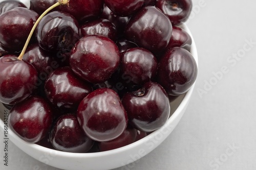 Fresh dark cherries in ceramic bowl on neutral gray cloth – minimal food photography