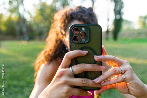 close up of two female hands holding a cell phone taking a photograph outdoors