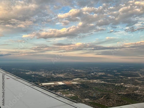 Aerial late afternoon view of suburban neighborhoods, roads, and development patterns with partly cloudy sky, showing organized residential layout from above