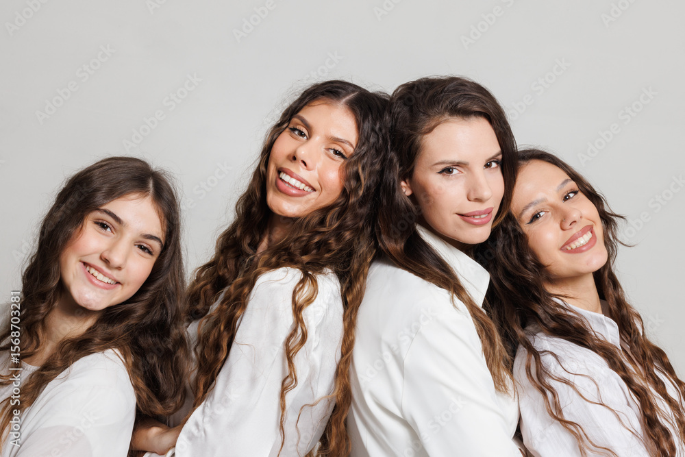 Four cheerful women with curly hair posing together in white clothing against a light background. Four cheerful women with curly hair posing together in white clothing against a light background.