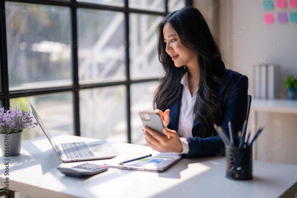 A woman is sitting at a desk with a laptop and a cell phone A woman is sitting at a desk with a laptop and a cell phone