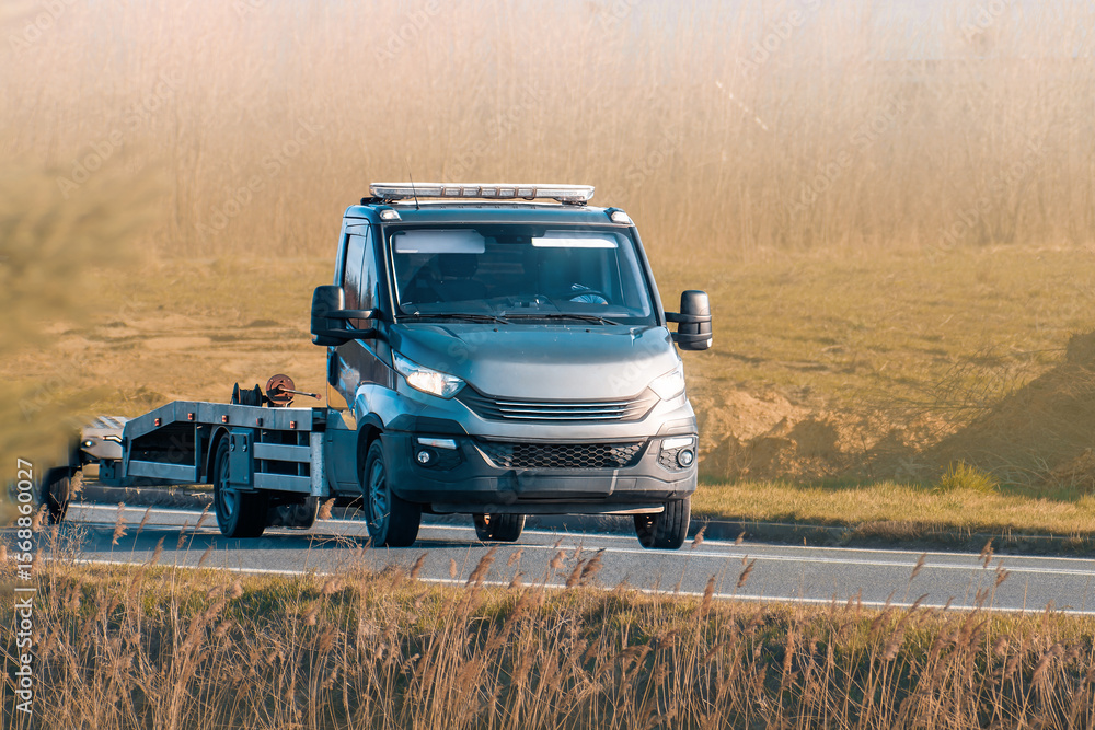 Fototapeta premium Orange tow truck driving on country road