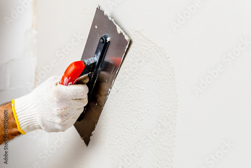 A hand in a glove is smoothing plaster on a wall with a trowel