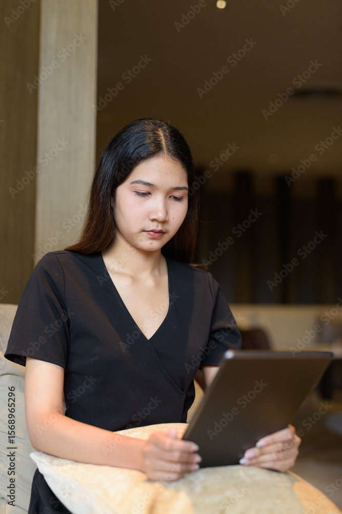 Young Asian woman sitting in coffee shop wearing black dress using tablet computer Young Asian woman sitting in coffee shop wearing black dress using tablet computer