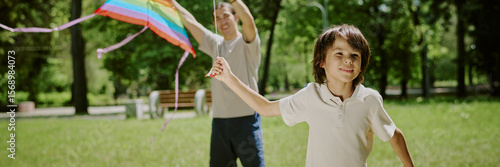 Behang Biracial boy running with colorful kite while middle aged Dad standing behind ho