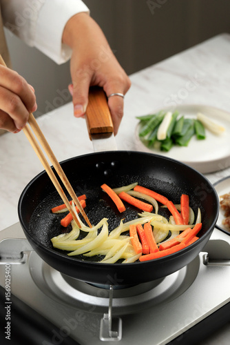 Foto Female Hand Sauteed Onion and Carrot on Black Pan