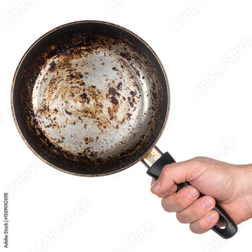 A hand holds a heavily stained and rusted frying pan with a black handle, showing significant wear and discoloration inside the pan.