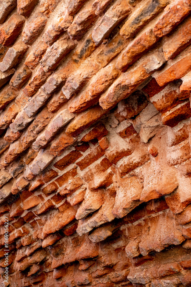 Fototapeta premium A close-up of a beat-up red brick wall with rough, uneven bricks in shades of red, orange, and brown, showing off years of wear and tear.