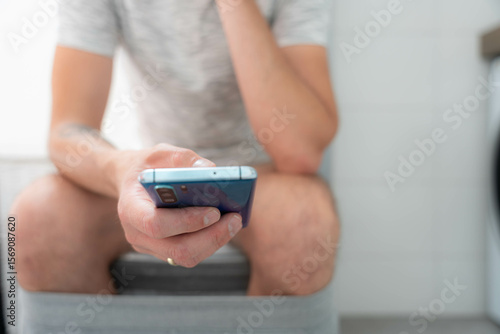 Photos Man using smartphone while seated on toilet in modern bathroom showcasing digita