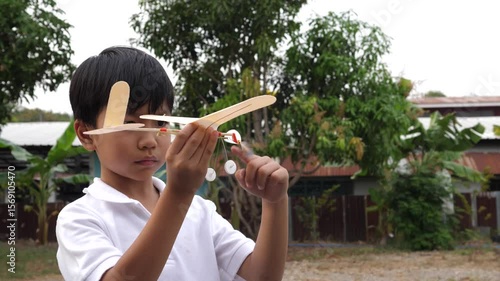 Asian child boy play airplane toy outdoor with fun face in nature background. Happy kid in white shirt enjoy playing in relaxing day.