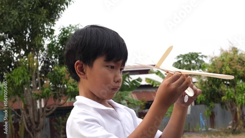 Asian child boy play airplane toy outdoor with fun face in nature background. Happy kid in white shirt enjoy playing in relaxing day.
