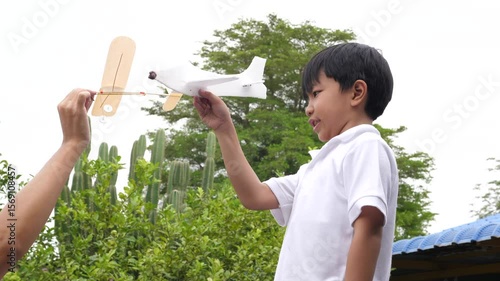 Happy family asian child boy and father play airplane toy outdoor together with fun face in nature background. Happy kid and dad in white shirt enjoy playing in relaxing day.