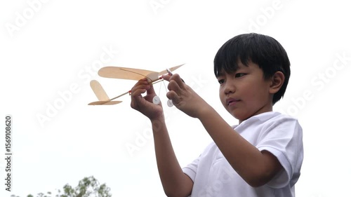 Asian child boy play airplane toy outdoor with fun face in nature background. Happy kid in white shirt enjoy playing in relaxing day.