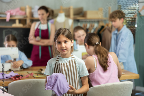 Teenage girl happily shows off a t-shirt he sewed with his own hands on a sewing machine