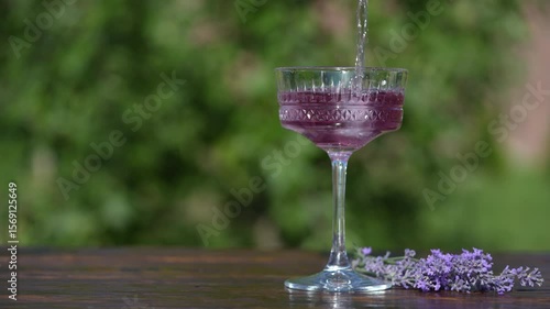 Bright summer cocktail or lemonade in crystal glass against  summer garden background on wooden table, close up. Drink with lavender herb flowers. Delicious alcoholic drink for relax on sunny day